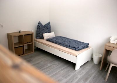 Schlafzimmer der DBT-A Wohngruppe mit Bett, Schreibtisch und Nachtkästchen.