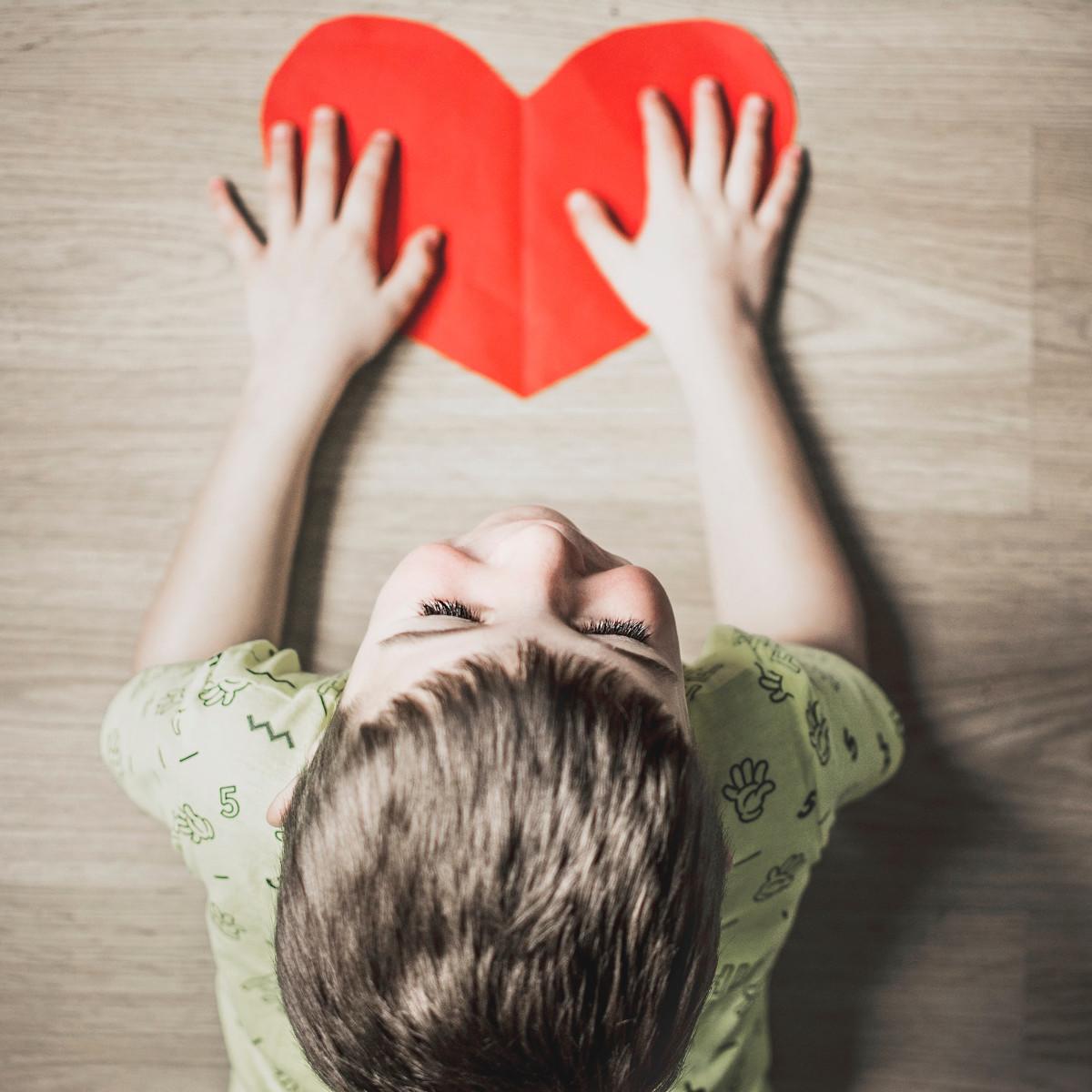 Ein Kind liegt auf dem Bauch und hat beide Hände auf ein selbst gemaltes Herz gelegt.